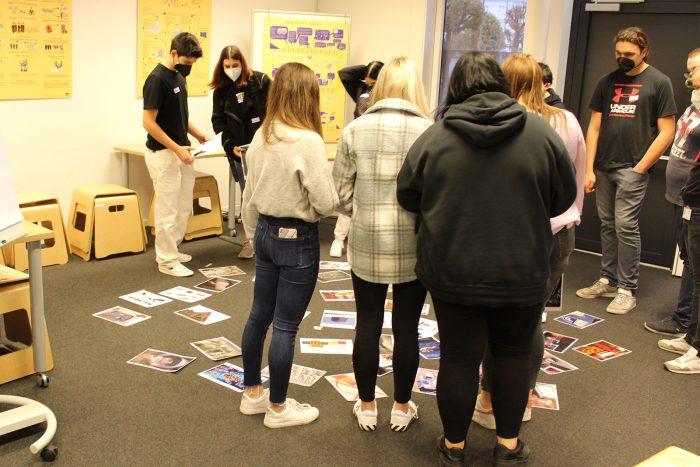 Lehrlinge stehen im Raum und betrachten bunte Karten die am Boden liegen