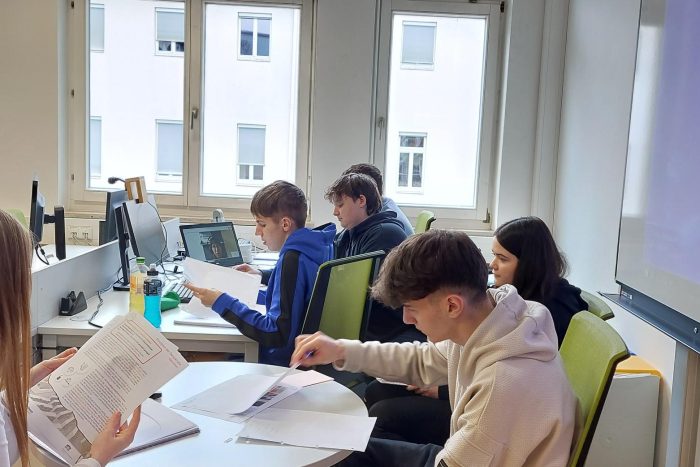 2 Lehrlinge sitzen auf Sesseln vor einem Tisch mit Unterlagen und zeichnen.