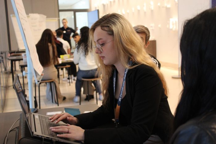 1 Lehrling sitzt vor einem Tisch und schreibt auf einem Laptop.