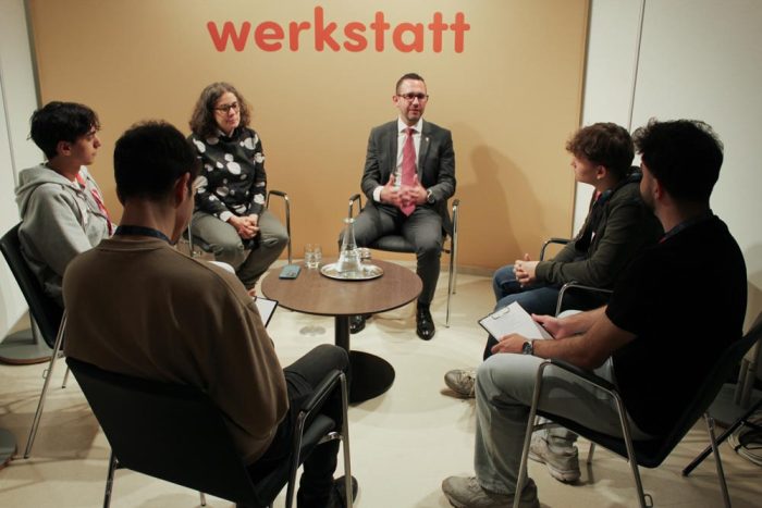 Vier Lehrlinge und zwei Politiker:innen sitzen auf Sesseln um einen Tisch und reden miteinander