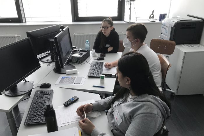 Drei Lehrlinge sitzen an einem Tisch und arbeiten am Computer