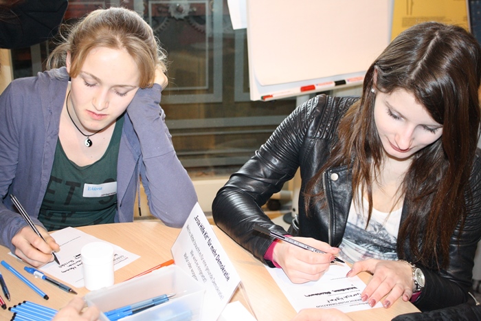 Zwei junge Frauen der Lehrlingsgruppe schreiben Ideen auf