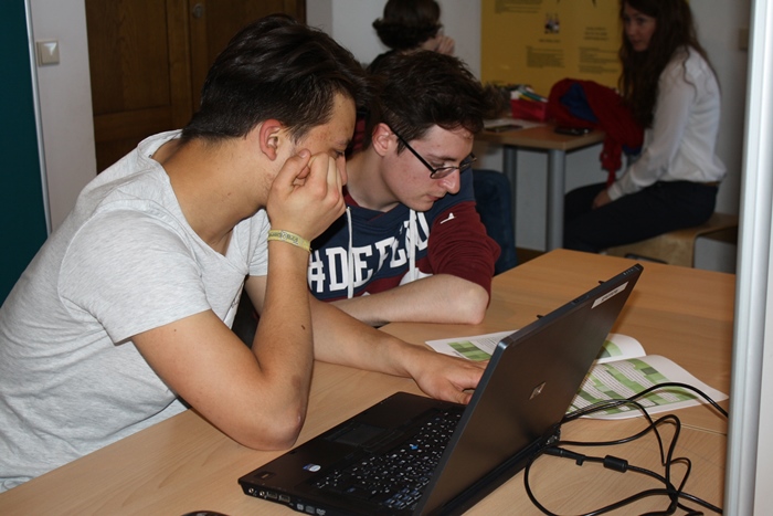 Zwei Lehrlinge recherchieren, vor einem Laptop sitzend, in einer Zeitschrift