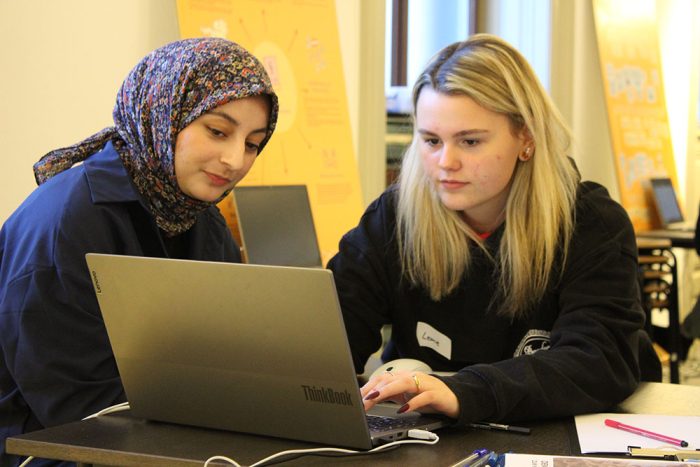 Zwei Lehrlinge sitzen vor einem Tisch mit einem Laptop darauf, ein Lehrling schreibt